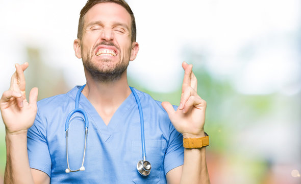 Handsome doctor man wearing medical uniform over isolated background smiling crossing fingers with hope and eyes closed. Luck and superstitious concept.