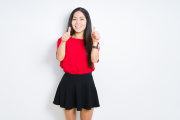 Fototapeta premium Beautiful brunette woman wearing red t-shirt and skirt over isolated background approving doing positive gesture with hand, thumbs up smiling and happy for success. Looking at the camera