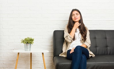 Young arab woman sitting on the sofa suffers pain in throat due a virus or infection.