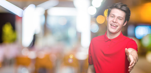 Young handsome man wearing red t-shirt over isolated background smiling friendly offering handshake as greeting and welcoming. Successful business.
