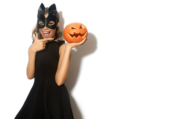 Happy young women in little black dress with Halloween pumpkin and in cat mask over white background