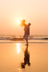 Fototapeta na wymiar Romantic happy couple in love hugging and spinning at sunset beach, silhouettes of young man and woman on holidays or honeymoon 