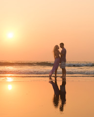 Fototapeta premium Silhouettes of young couple in love having a great time on the honeymoon staying on the beach with beautiful red sunset on background