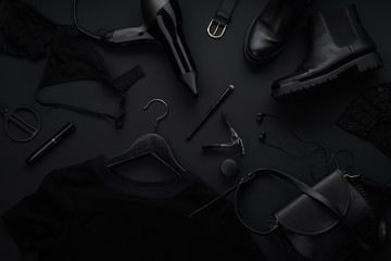 Black monochromatic flatlay on black background. Clothes, accessories and beauty equipment. Black...