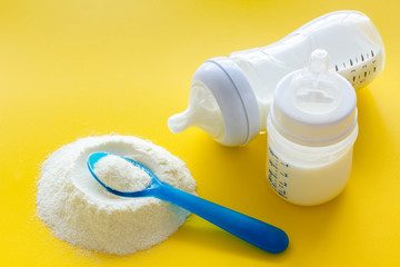 Baby food. Powder in spoon near baby bottle on yellow background copy space