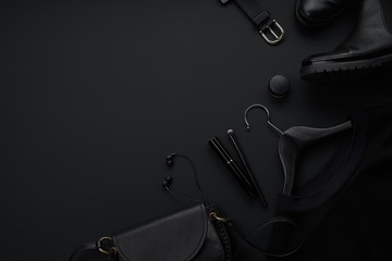Black monochromatic flatlay on black background. Clothes, accessories and beauty equipment. Black friday sale concept. Copy space