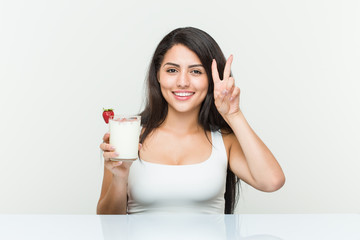 Young hispanic woman holding a smoothie young hispanic woman holding an avocado toast showing victory sign and smiling broadly.< mixto >