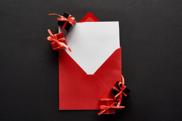 top view of blank card in red envelope near presents on black background