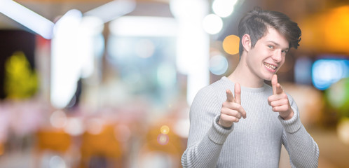 Young handsome man wearing winter sweater over isolated background pointing fingers to camera with happy and funny face. Good energy and vibes.