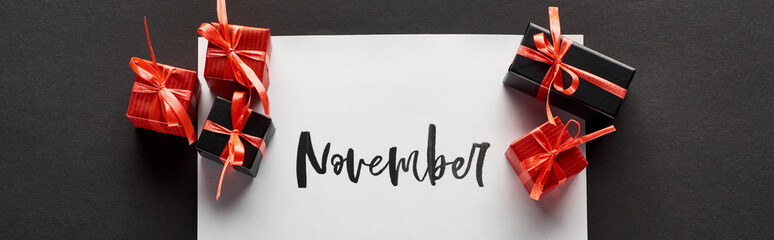 top view of gift boxes and paper with November lettering on black background, panoramic shot