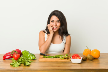 Young curvy woman preparing a healthy meal biting fingernails, nervous and very anxious.