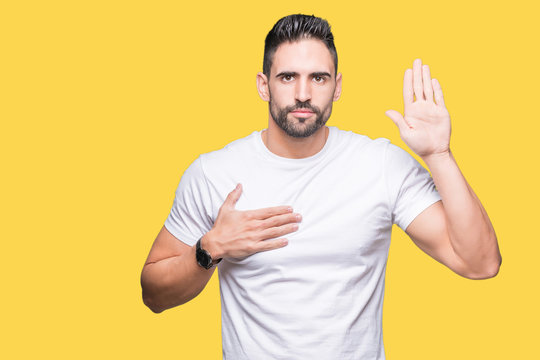 Handsome man wearing white t-shirt over yellow isolated background Swearing with hand on chest and open palm, making a loyalty promise oath
