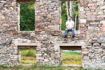 young man relaxing with coffee outdoors in window of abandoned building