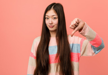 Young cool chinese woman showing a dislike gesture, thumbs down. Disagreement concept.