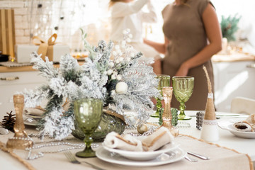 Beautiful served table with decorations, candles with glaze on white tablecloth on the background of the kitchen with people. Living room