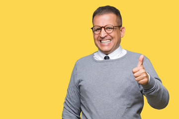 Middle age bussines arab man wearing glasses over isolated background doing happy thumbs up gesture with hand. Approving expression looking at the camera showing success.