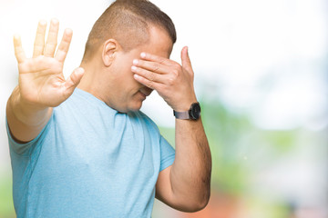Middle age arab man wearing blue t-shirt over isolated background covering eyes with hands and doing stop gesture with sad and fear expression. Embarrassed and negative concept.
