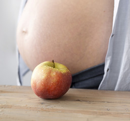 Pregnant woman next to apple on table close-up