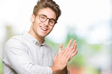 Young handsome man wearing glasses over isolated background Clapping and applauding happy and joyful, smiling proud hands together