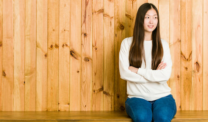 Young chinese woman sitting on a wooden place smiling confident with crossed arms.