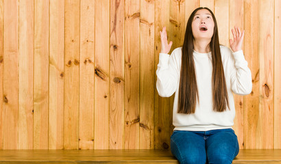 Young chinese woman sitting on a wooden place screaming to the sky, looking up, frustrated.