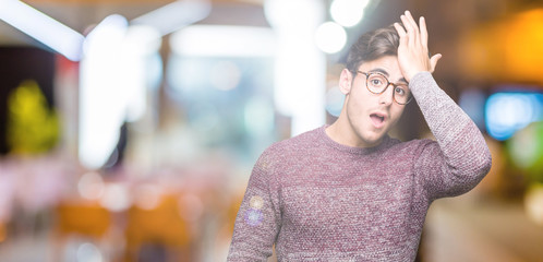 Young handsome man wearing glasses over isolated background surprised with hand on head for...