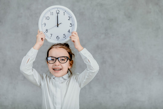 Beautiful little girl with a clock on a gray background. Lift his hands up with the clock. Emotional
