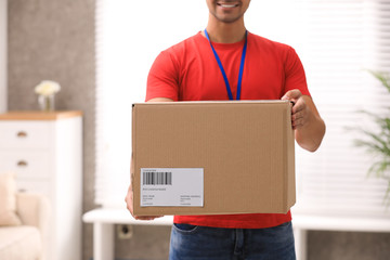 Young courier holding parcel indoors, closeup. Delivery service