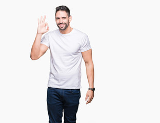 Young man wearing casual white t-shirt over isolated background smiling positive doing ok sign with hand and fingers. Successful expression.