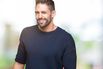Obraz premium Young handsome man wearing sweater over isolated background winking looking at the camera with sexy expression, cheerful and happy face.