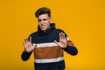 Young cool man wearing a hoodie rejecting someone showing a gesture of disgust.