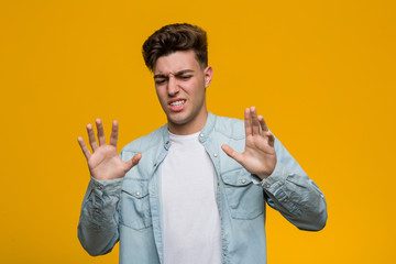 Young handsome student wearing a denim shirt rejecting someone showing a gesture of disgust.