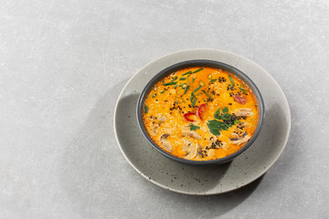 Tom Yam kung Spicy Thai soup with shrimp, seafood, coconut milk and chili pepper in bowl. In gray stone background. Horizontal photo.