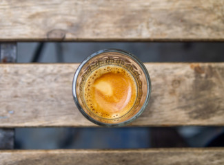 a small glass expresso coffeee under a defocus wood table on a esplanade