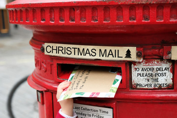 Child is posting a letter for Santa Claus into the Christmas english postbox. Popular children Christmas activity. 