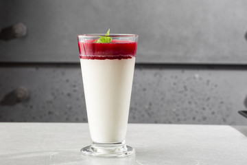 Delicious italian dessert panna cotta with berry sauce and mint on gray background. Traditional italian dessert. Horizontal photo.
