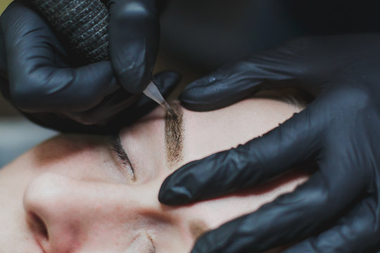 master in black gloves makes permanent eyebrow makeup close-up 1