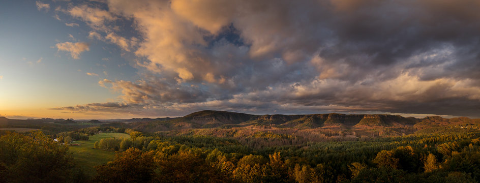 Autumn landscape at sunset - mountains, forests and beautiful clouds illuminated by the setting sun, hills of Bohemian Switzerland and Saxon Switzerland National Park, Czech Republic and Germany