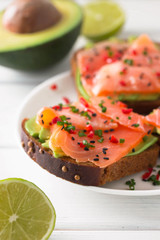 Sandwich with salmon, avocado, sesame, lime and chili pepper on a white wooden background.