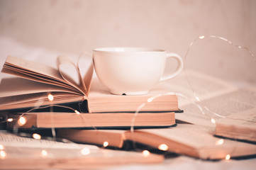 Cup of coffee with folded book pages in heart shape staying on open books in stack closeup. Selective focus. WInter holiday season.