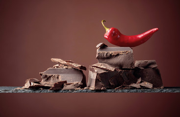 Black chocolate with red pepper on a brown background.