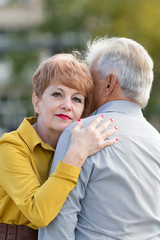 An elderly wife hugs her husband with a gray head. A gray-haired man with his wife on the street.