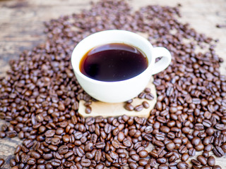 A cup of black cofee and Coffee beans are on the wooden table, ready to give freshness and alongside the businessman