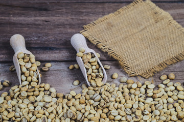 Organic Raw coffee beans in wood spoon on wood table.
