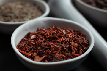 Spice red paprika in a white ceramic bowl next to a pounder on a black background