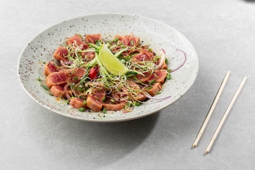 Close up of rare seared tuna slices with lime and arugula leaves on a plate. Gray background. Tuna salad. Top view from above horizontal.