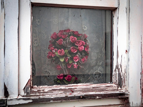 Plastikblumen hinter altem Holzfenster