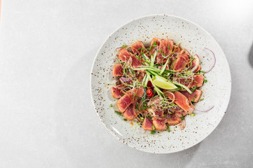 Close up of rare seared tuna slices with lime and arugula leaves on a plate. Gray background. Tuna salad. Top view from above horizontal.