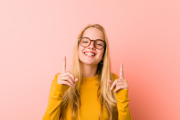 Adorable teenager woman indicates with both fore fingers up showing a blank space.