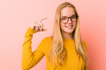 Adorable teenager woman holding something little with forefingers, smiling and confident.